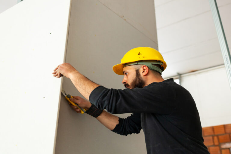 Un ouvrier pose du placo sur un mur en pierre