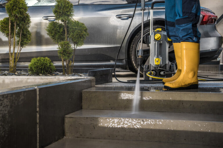 Un homme portant une botte en nettoyant l'allée près d'une voiture avec un karcher