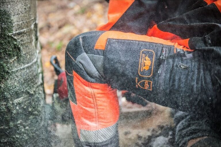 Un bûcheron tronçonne un arbre avec un pantalon anti-coupure comme équipement de protection individuelle (EPI)