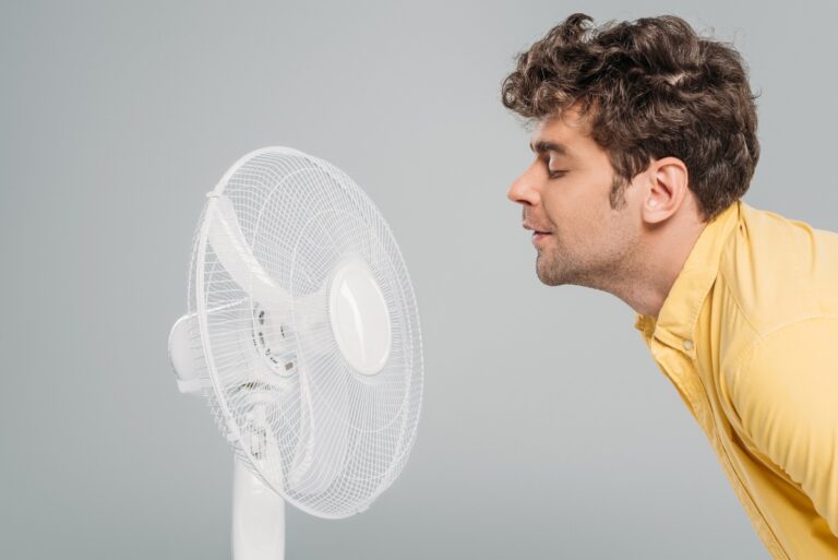 Un homme aspirant l'air du ventilateur pendant que la chaleur dans sa maison monte