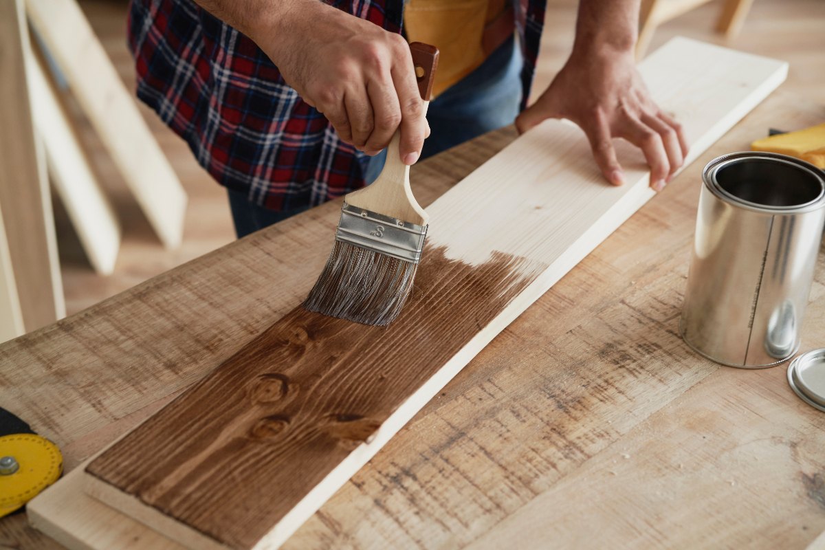 Une personne qui utilise un pinceau pour peindre le bois avec de l'huile de vidange