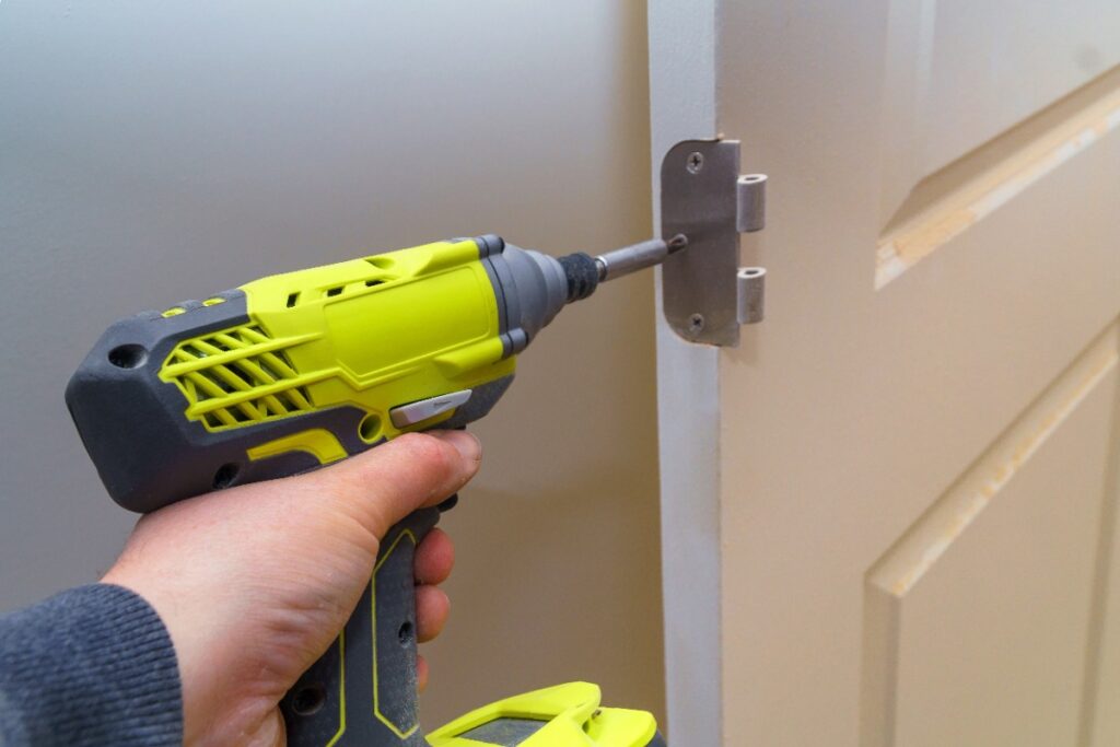 Main d'un homme qui pose un fiche à visser sur une porte