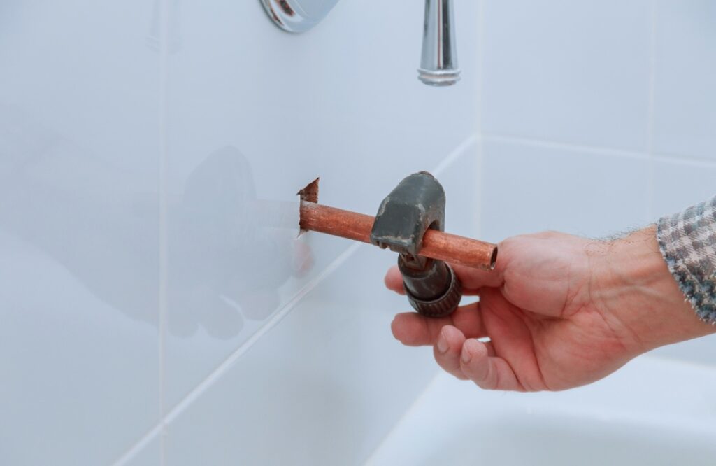 Une personne tenant un coupe-tube en coupant un tuyau en cuivre