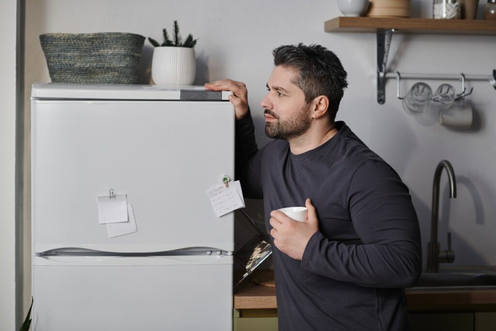 Un homme qui se tient debout à côté de son frigo