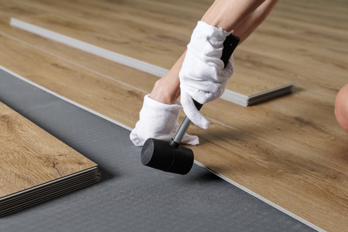 Des mains avec des gants assemblant un revêtement de sol en plancher