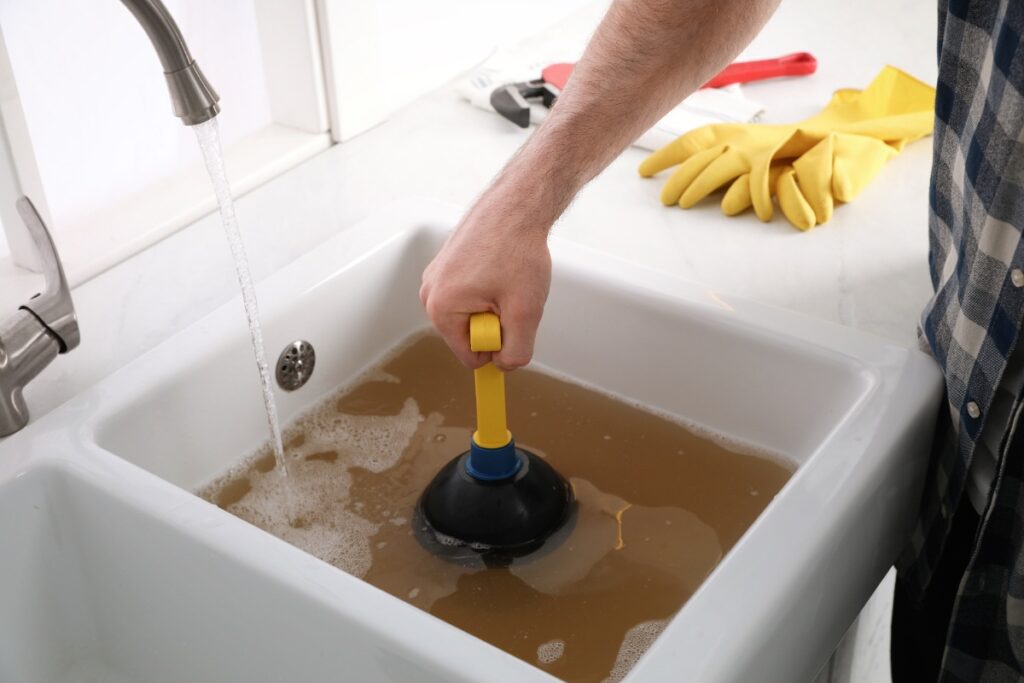 Un évier bouché avec de l'eau sale et une personne qui tient une ventouse dedans