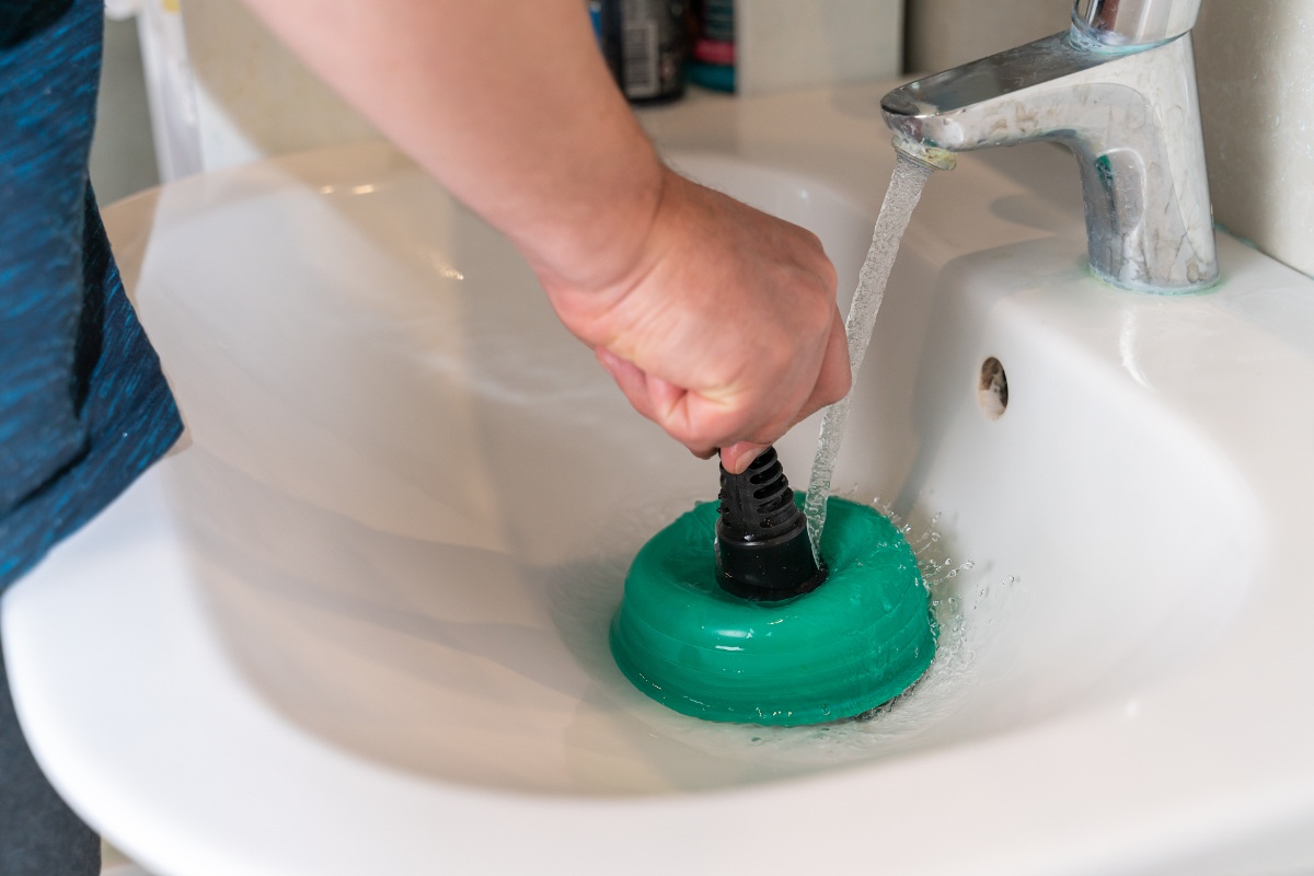 Main d'une personne utilisant une ventouse pour boucher le lavabo