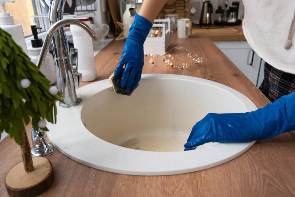 Des mains avec des gants nettoyant l'évier de cuisine