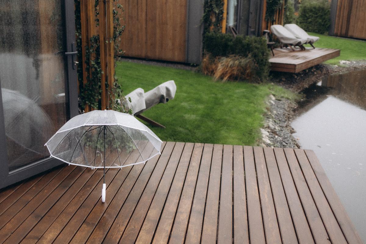 Un parapluie transparent posé sur une terrasse en bois sous la pluie