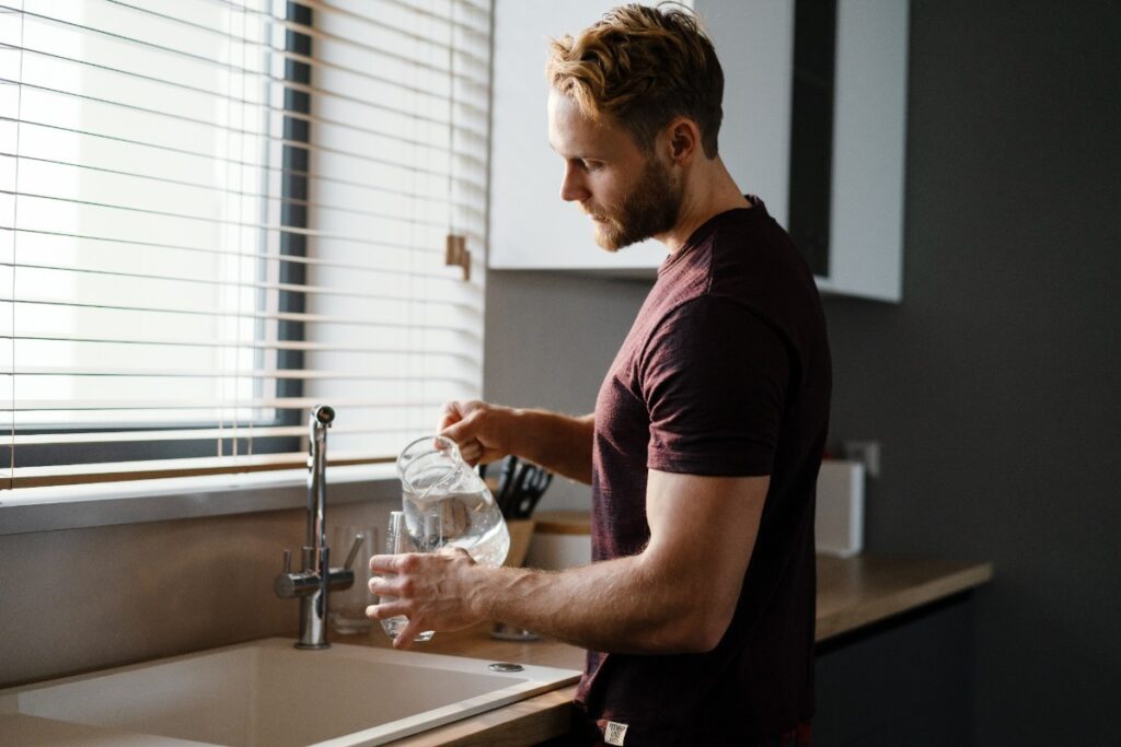 Un homme qui verse de l'eau du carafe dans un verre d'eau
