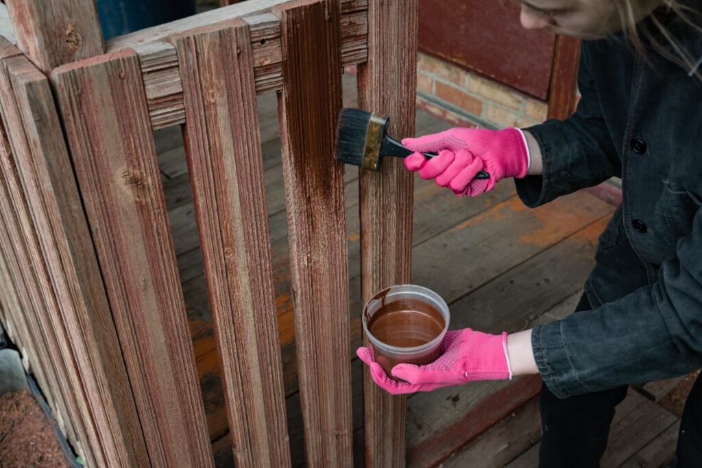 Une personne appliquant de la teinture sur une clôture en bois