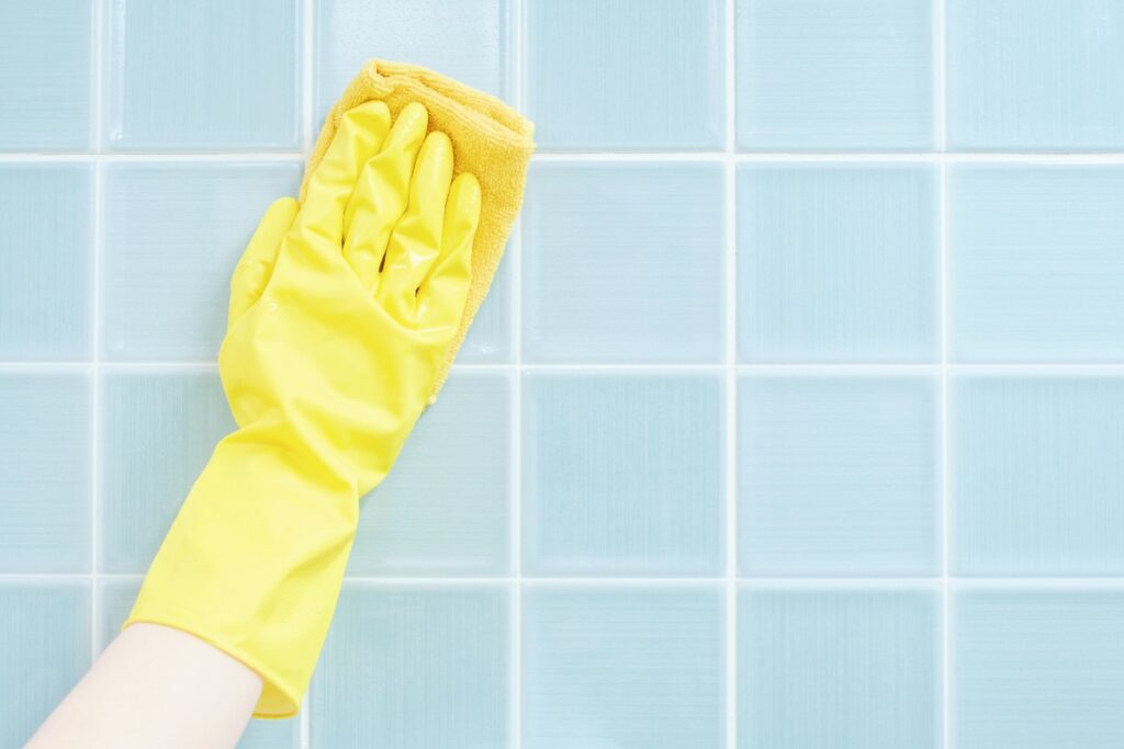 Main avec un gant jaune qui essuie du carrelage