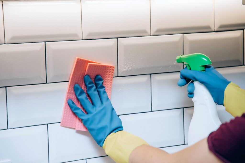 Mains gantées nettoyant le mur carrelé avec une éponge