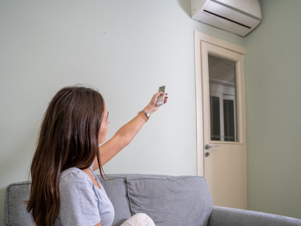Une femme réglant le climatiseur dans sa maison