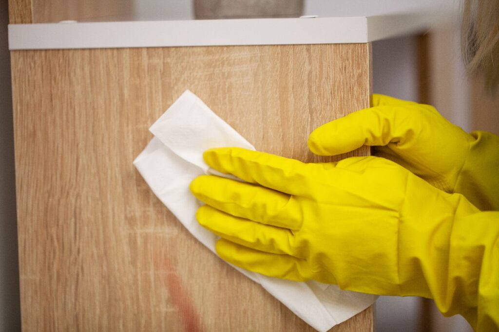 Mains gantées essuyant la poussière sur du meuble en bois