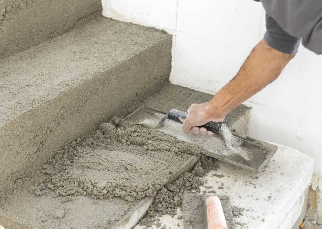 Un ouvrier du bâtiment appliquant du ciment sur la marche de l'escalier